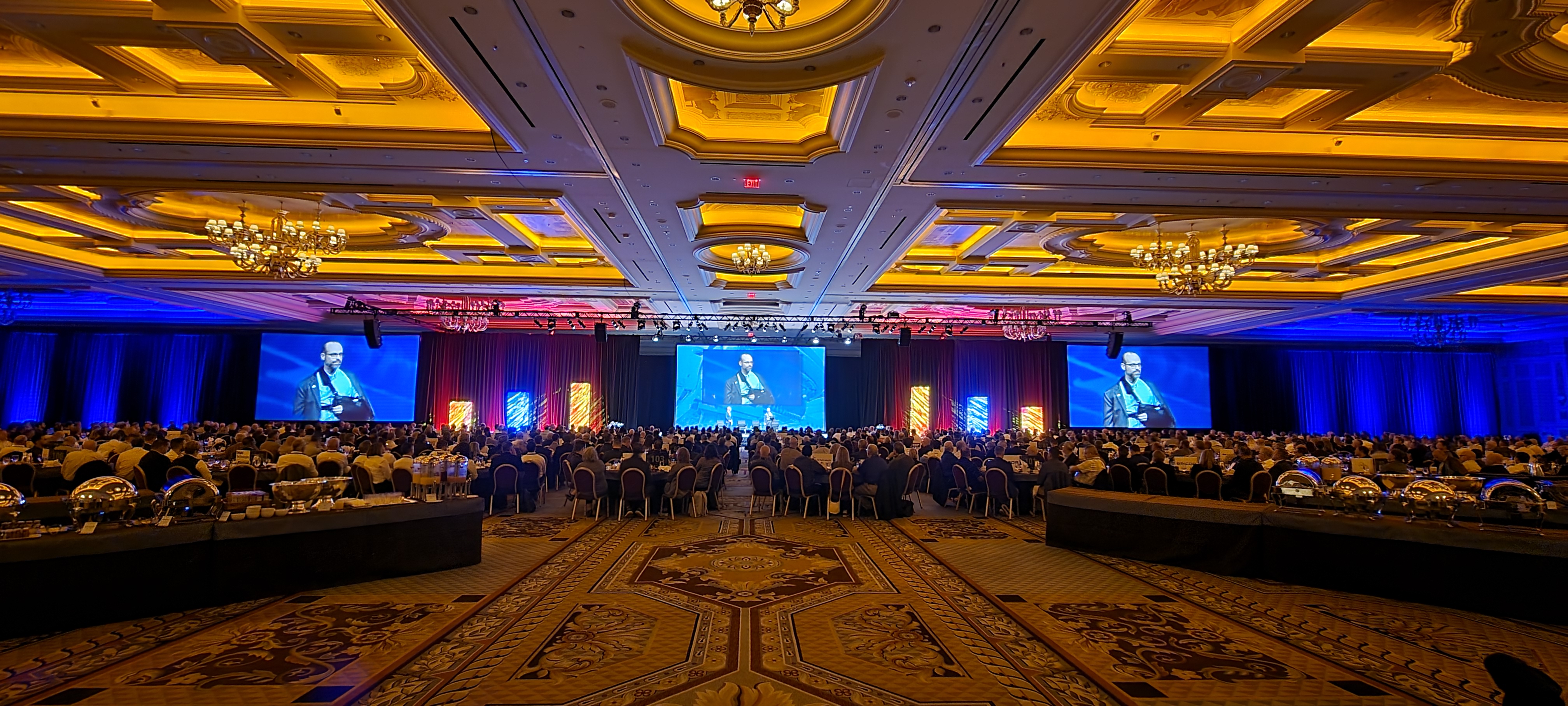 Grand ballroom corporate gala with IMAG screens and hundreds of attendees